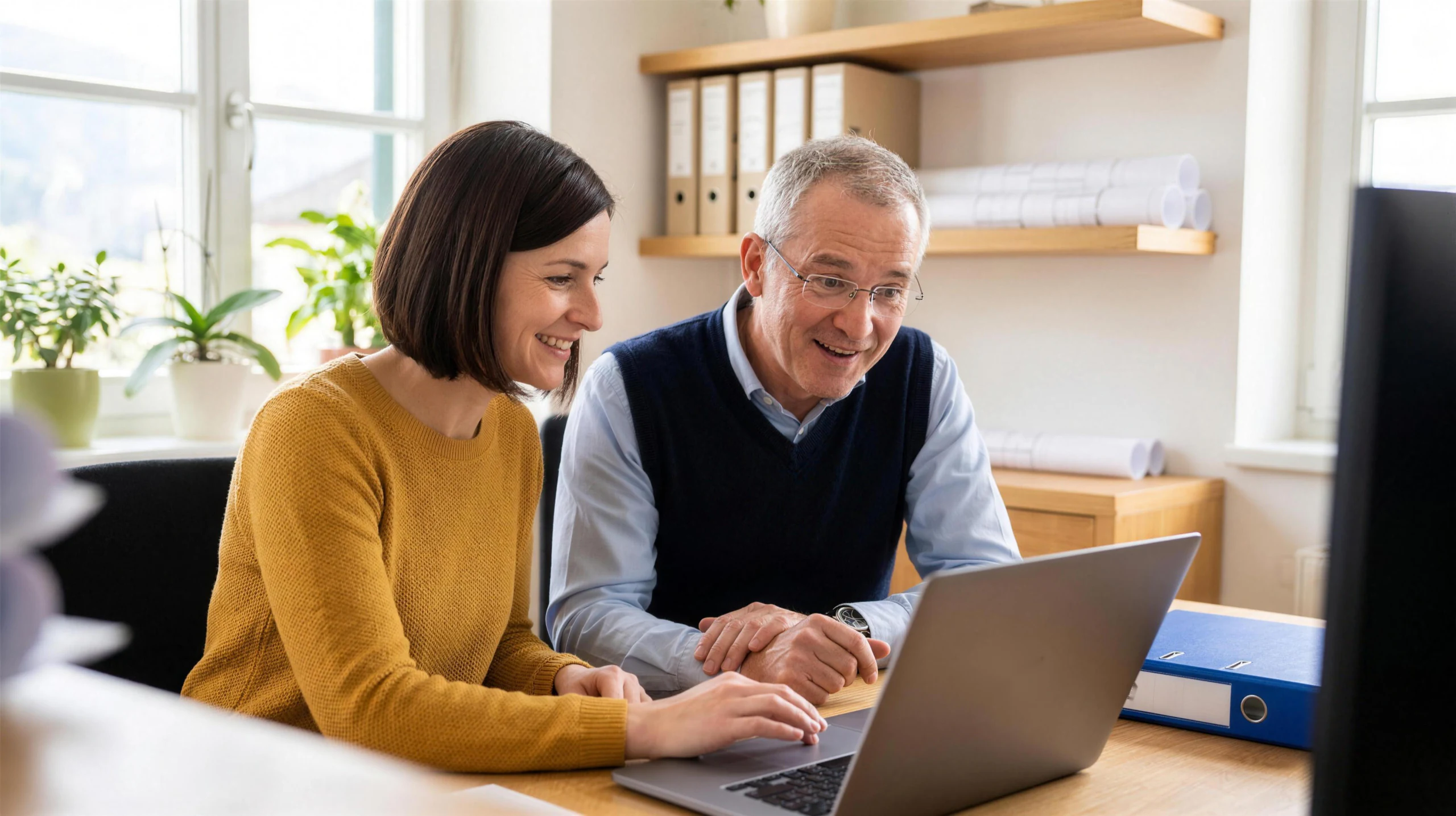 Eine Mitarbeiterin und ihr Kollege freuen sich am Laptop über die schnelle Antwort zu ihren Projekten